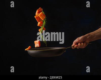 The process of cooking pieces of salmon, tuna, trout in a pan on a black background by a professional chef. Levitation. Fish and seafood cooking recip Stock Photo