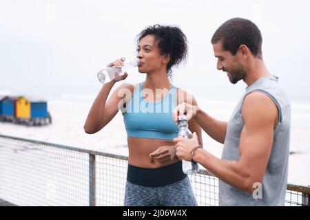 Ensure you drink enough water before, during and after exercising. Shot of two sporty young people drinking water while exercising outdoors. Stock Photo