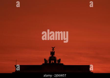 Berlin, Germany. 17th Mar, 2022. Colorful is the sky above the Brandenburg Gate for a moment at sunrise. Credit: Paul Zinken/dpa/Alamy Live News Stock Photo
