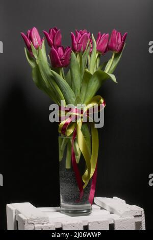 Bouquet of burgundy tulips in a vase. It's on a box. On a black background. Stock Photo