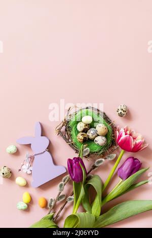 Pink and purple tulips with colorful quail eggs in a nest over pink background. Spring and Easter holiday concept. Top view flat lay. Stock Photo