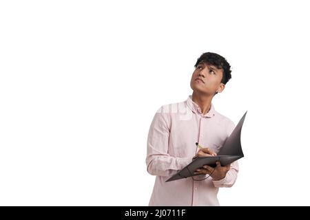 Young peruvian man looking up and writing on a folder with a pen, isolated. Stock Photo