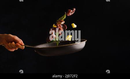 Seafood, vegetables, herbs and lemon slices in a frying pan in a frozen flight on a black background. Sea food, seafood dishes. Delicious healthy vege Stock Photo