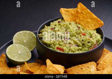 Guacamole dip with tortilla chips or nachos and lime on a black background Stock Photo