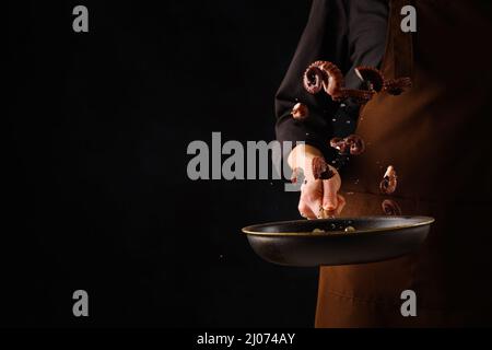 Chef roasts octopus pieces in frying pan. Concept of cooking seafood kitchen.On black background with empty space for inscription. recipe book.Asian c Stock Photo