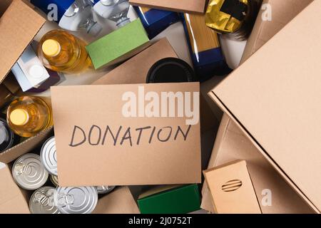 Food donations boxes with grocery products and card with inscription Donation on the table. Cardboard boxes with oil, canned food, cereals, pasta Stock Photo