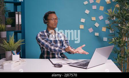 Call center operator having argument with client on helpline using headset with microphone and laptop at desk. Telemarketing employee yelling at person at customer support service. Stock Photo