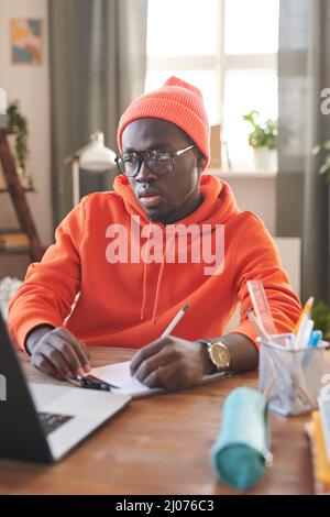 Medium portrait of serious male college student sitting at desk in front of laptop doing homework Stock Photo
