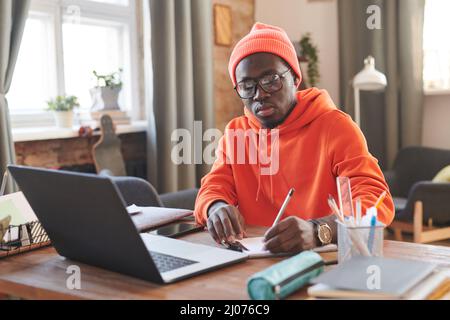 Portrait of young male college student sitting at desk in front of laptop making notes Stock Photo