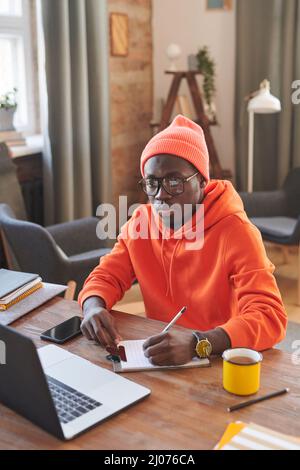 Vertical high angle view shot of modern college student wearing stylish orange clothes working on assignment at home Stock Photo