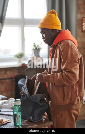 Side view portrait of stylish African American male student wearing casual outfit getting ready for school putting textbooks and into backpack Stock Photo