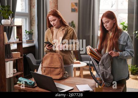 Horizontal medium shot of modern young female twins getting ready for school putting textbooks and copybooks into backpacks Stock Photo