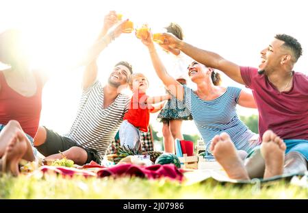 Multicultural families having fun together with kids at pic nic camping party - Joy and love life style concept with young mixed age people toasting j Stock Photo