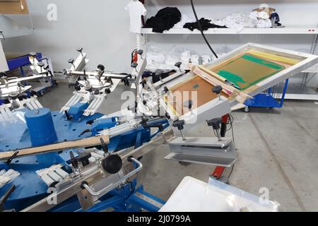 Screen printing machine for applying images by silkscreen printing. Print screening apparatus. Serigraphy production. Printing images on t-shirts in a Stock Photo