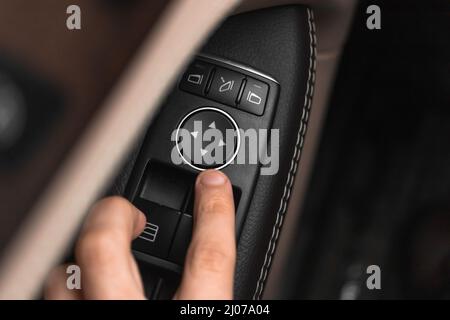Close-up hand pressing button automatic power controlling window in car. Modern luxury car interior with leather background Stock Photo