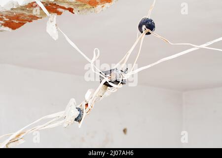 Home repair and renovation . Replacing the eletricity wiring installation. Very old power plugs and cables hanging from the ceiling Stock Photo