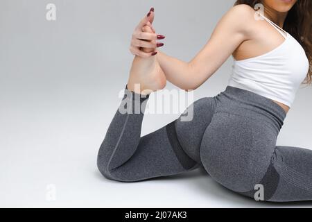 Young barefoot woman in leggings and pullover stretching legs