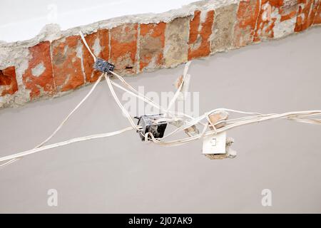 Home repair and renovation. Replacing the eletricity wiring installation. Very old power plugs, switch and cables hanging from a pulled down wall. Stock Photo