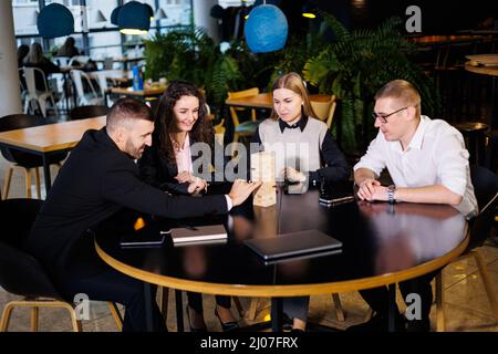 A company of colleagues in the office during a break plays the board game jenga. Fun board games for friends Stock Photo