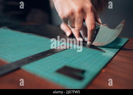 Tanner female hands cutting leather goods on workshop. Working process of leather craftsman. Stock Photo
