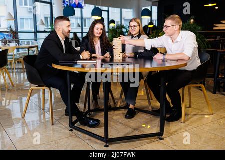 A company of colleagues in the office during a break plays the board game jenga. Fun board games for friends Stock Photo