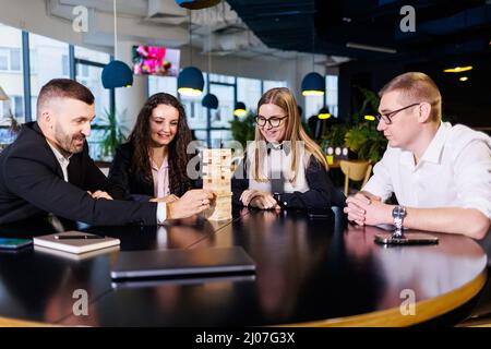 A company of colleagues in the office during a break plays the board game jenga. Fun board games for friends Stock Photo