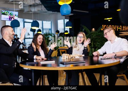 A company of colleagues in the office during a break plays the board game jenga. Fun board games for friends Stock Photo