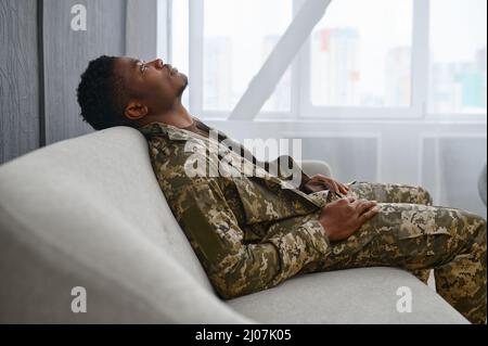 Depressed soldier in uniform sitting on couch Stock Photo