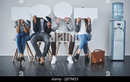Tell us a little more about yourself. Shot of a diverse group of businesspeople holding up speech bubbles while they wait in line. Stock Photo