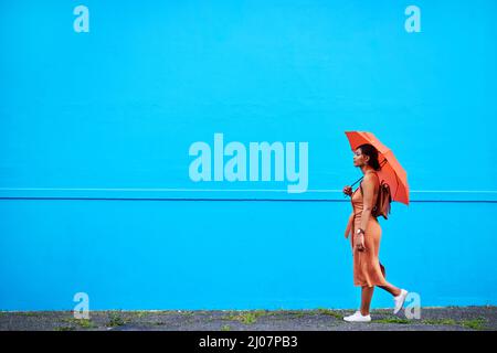 Always keep going forward in life. Full length shot of an attractive young woman holding an umbrella while walking against a blue background outdoors. Stock Photo