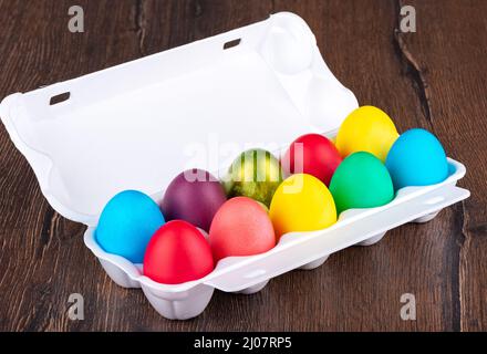 Multi-colored Easter eggs in a white plastic package on a wooden background. Close up. Stock Photo