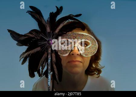 A woman hides her identity by holding a half mask or Columbina over her face. Stock Photo