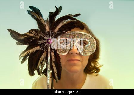 A woman hides her identity by holding a half mask or Columbina over her face. Stock Photo
