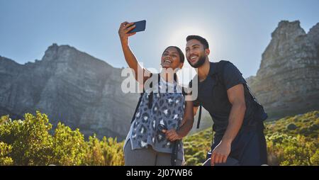 Soaking in all that vitamin D in the best way. Shot of a young couple taking photos while out on a hike in a mountain range outside. Stock Photo