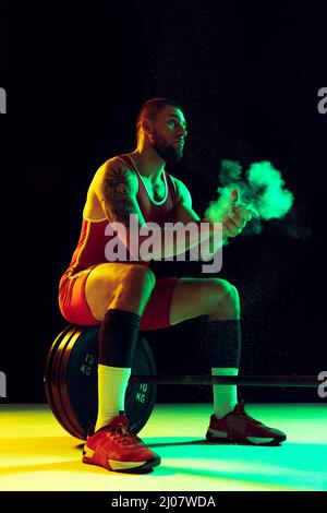 One young man, professional weightlifter sportswear training with barbell isolated dark background in neon. Sport, weightlifting, power, achievements Stock Photo
