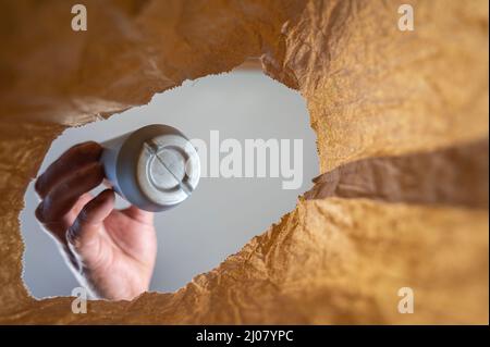 A hand retrieves a gray plastic bottle in a paper bag. A mature man's hand holds a sweet ice cream topping over an open brown bag. Shot from the botto Stock Photo