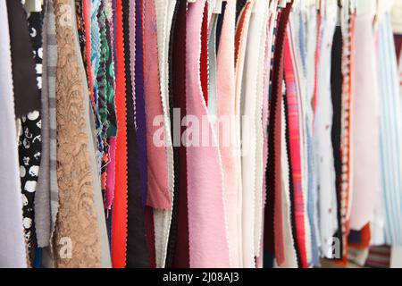 Colorful curtain samples hanging from hangers on rail in a clothes design studio. Multiple color fabric texture samples selection. Fabrics for clothes Stock Photo