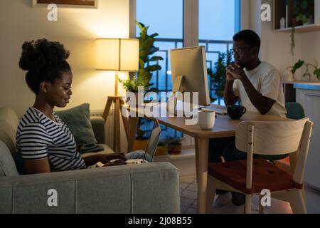 Young afro couple of freelancers work from home together busy with projects use computer and laptop Stock Photo