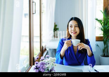 Manager, entrepreneur, female employee sitting and drinking coffee expressing a smiling face while taking a break from hard work. Stock Photo