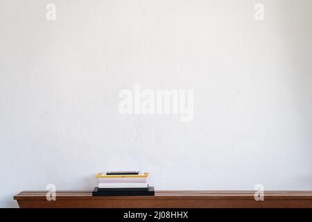 Pile of books on a wooden shelf against a white wall Stock Photo