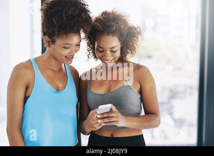 Making plans after yoga. Cropped shot of two young women looking at a cellphone after yoga class. Stock Photo