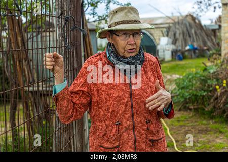An elderly woman wearing a hat and glasses speaks on İsimsiz Yol, Büyükkonuk, TRNC Stock Photo