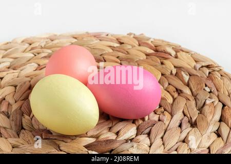 Easter colorful eggs in a basket on white wooden table. Burlap background. Happy Easter. Rustic, Eco concept. Dyed Eggs on a straw Napkin. Stock Photo