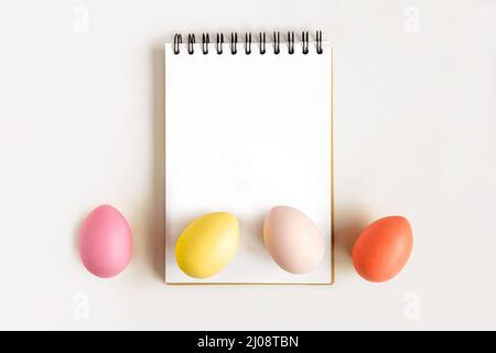 Notebook with Easter Eggs. Spiral notepad on spring white background. Top view of open writing pad with blank page, office flat lay. Easter Mock Up Stock Photo