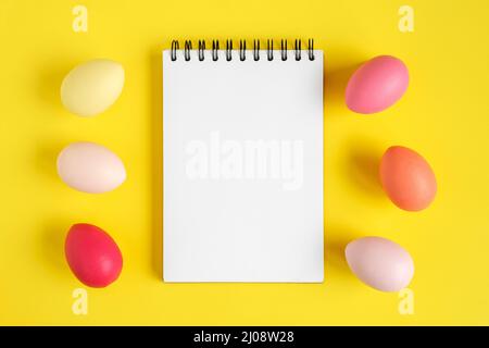 Notebook with Easter Eggs. Spiral notepad on spring yellow background. Top view of open writing pad with blank page, office flat lay. Easter Mock Up Stock Photo