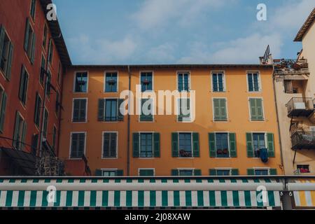 View over the market stalls of a traditional colourful apartment block building with wooden shutters on windows in the Old Town of Nice, France. Stock Photo