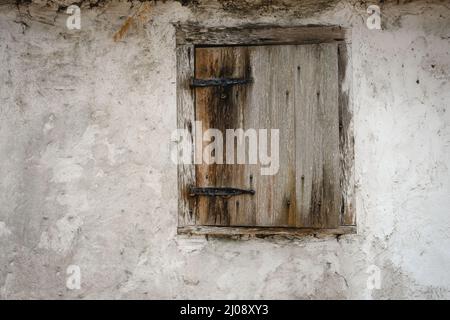 Ancient wood window shutter and black iron hinges set in wall made from wattle and daub Stock Photo