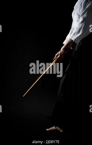 A girl in black hakama standing in fighting pose with wooden sword bokken over dark background. Shallow depth of field. SDF. Stock Photo