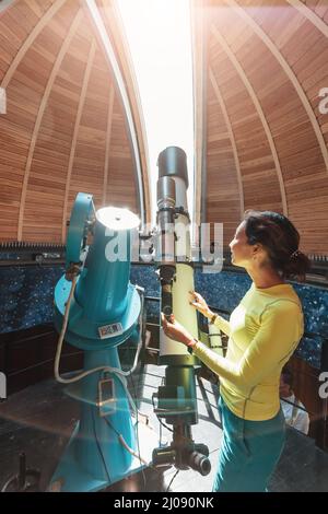 Happy woman in a space observatory looks at a meteorite or the sun through a professional optical telescope. Astronomy occupation and study concept Stock Photo