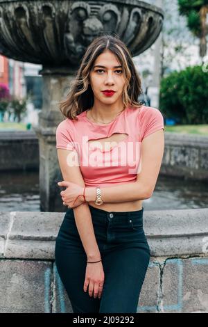 attractive young latin woman with her long wavy blonde hair, looking at the camera, wears makeup with red lips and shadows, youth fashion, beauty Stock Photo